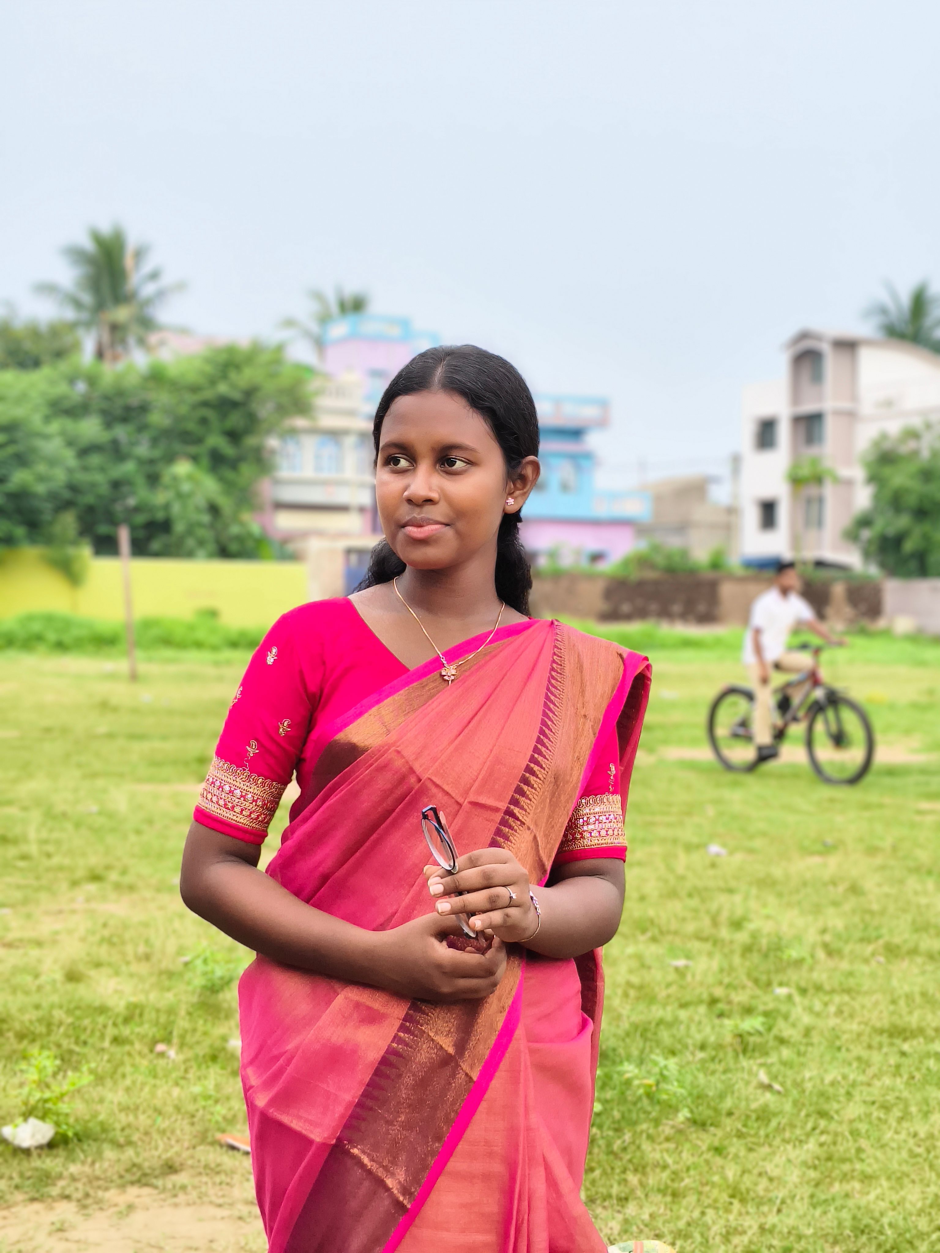 Young woman in a pink saree standing outdoors with building backdrop.