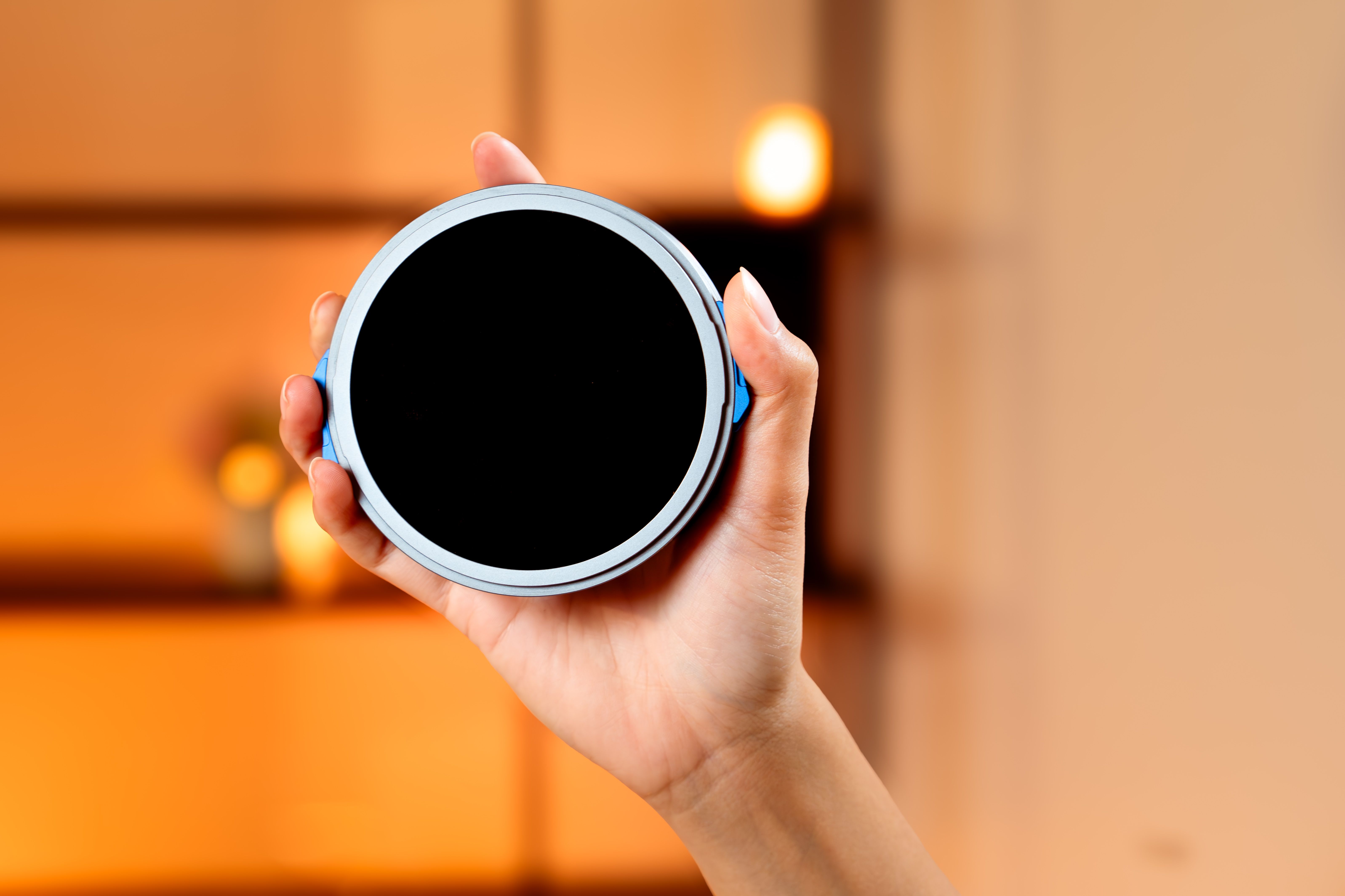 Close-up of a hand holding a circular black object against a warm orange blurred background.