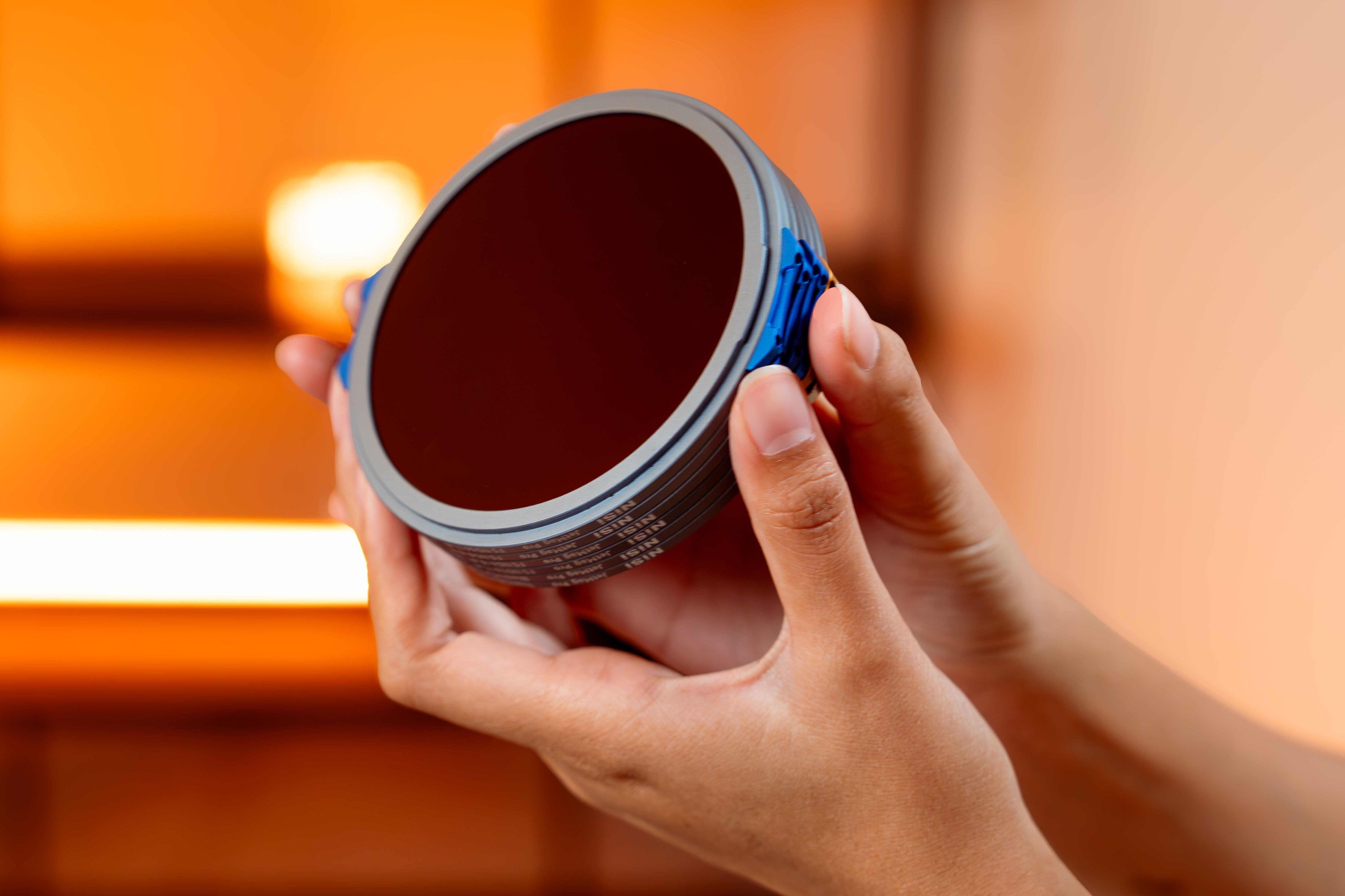 Hands holding a circular camera lens filter against a soft, warm background.