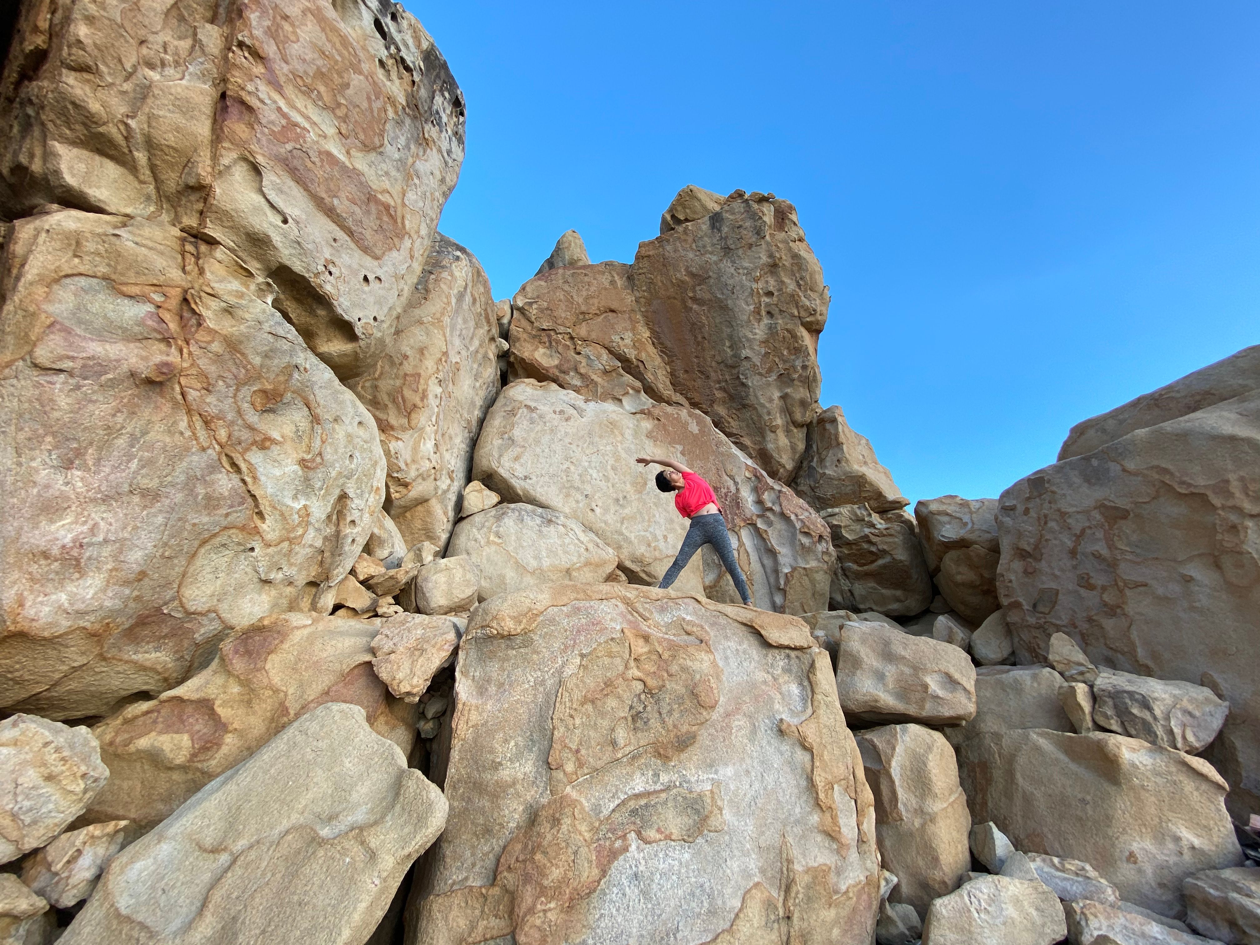 Person in red shirt climbing large rocky formation under blue sky. Outdoor adventure.