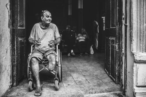 Free A black-and-white image capturing an elderly man in a wheelchair at a doorway in Havana, Cuba. Stock Photo
