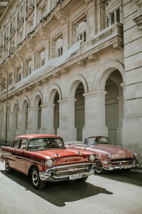 Free Vintage American cars parked on a street in Old Havana, Cuba, under an elegant colonial building. Stock Photo