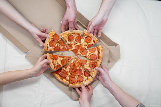 Multiple hands reaching for pepperoni pizza on a table, symbolizing sharing and enjoyment.