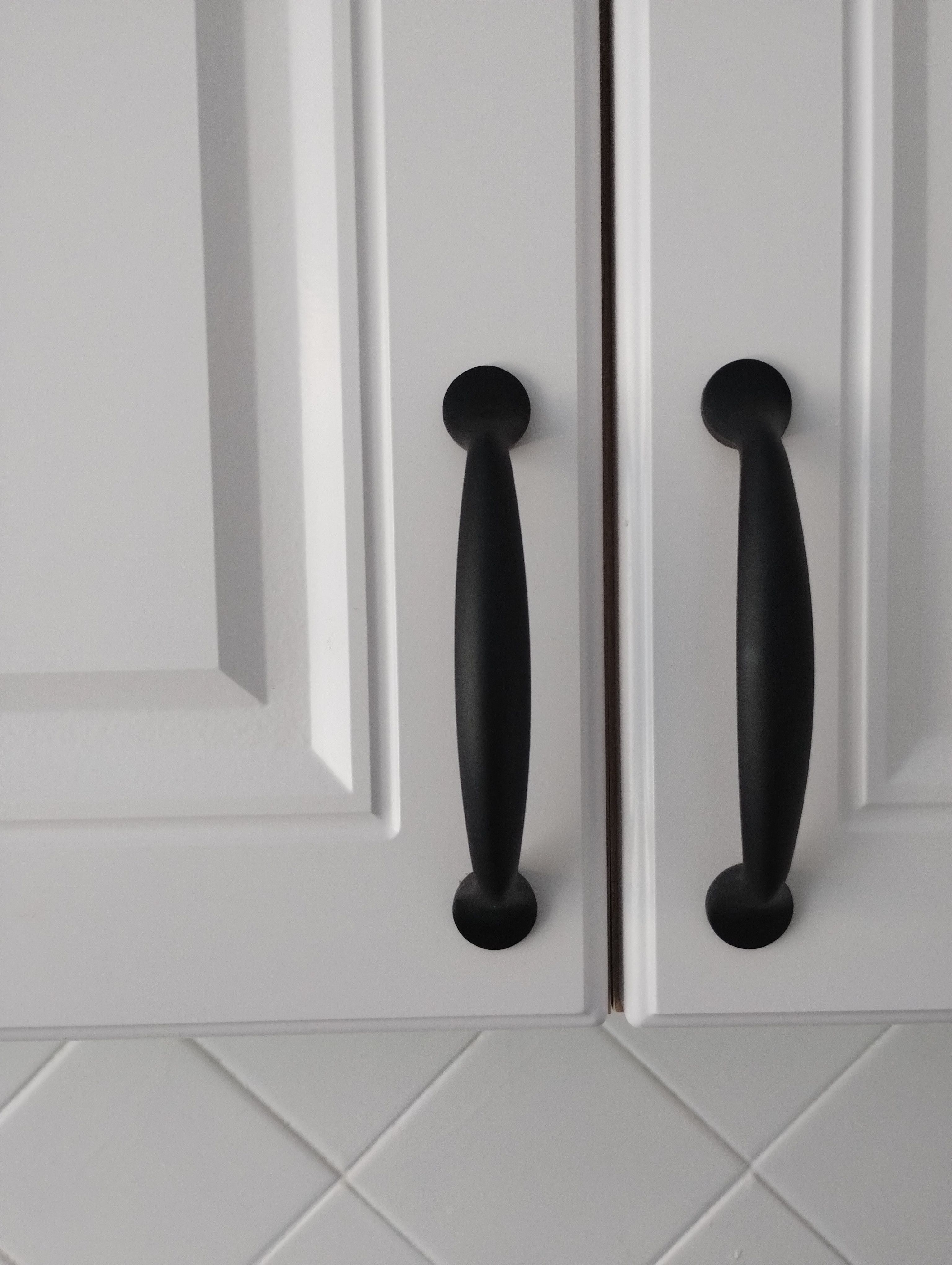 Modern black cabinet handles on white kitchen cabinets offer sleek, minimalist design.