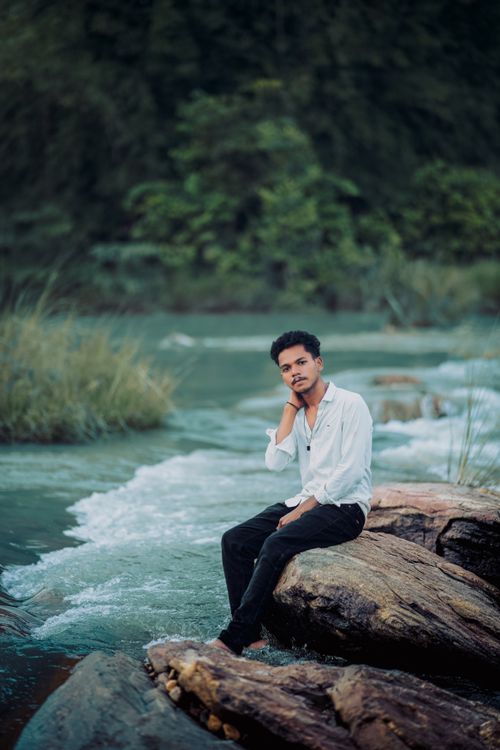 Free Portrait of a young man by a scenic river in Odisha, surrounded by lush vegetation and rocks. Stock Photo