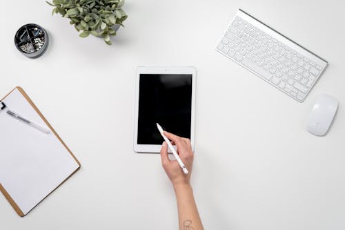 Person Holding White Ipad Near White Apple Keyboard