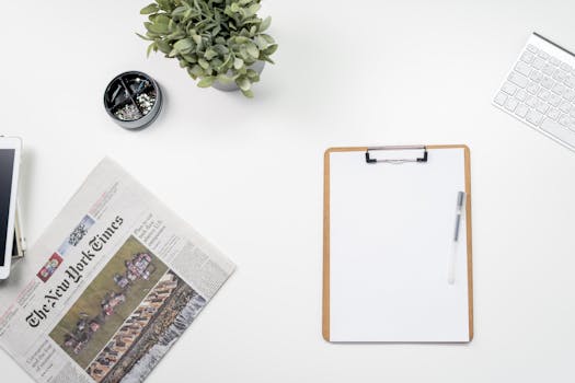 Top view of a minimalist home office desk setup with newspaper, keyboard, and clipboard.