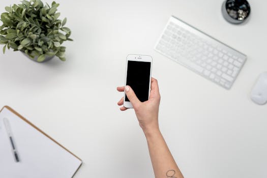 A modern workspace with a smartphone, keyboard, and plant, ideal for home office use.