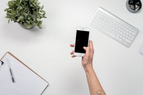 Free A clean and minimalist home office setup featuring a smartphone, keyboard, and plant. Stock Photo