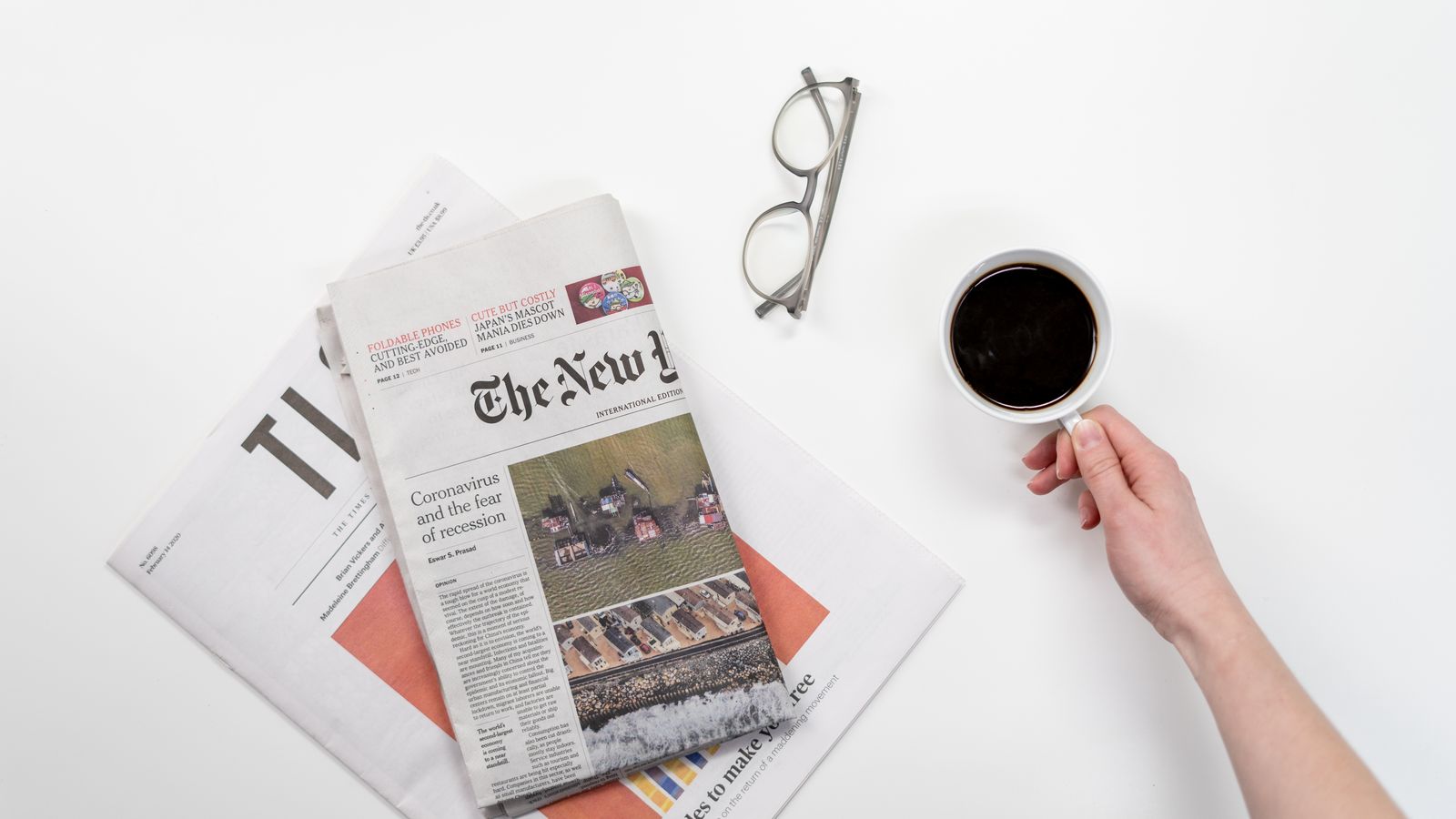 Top view of a coffee cup, newspapers, and eyeglasses on a clean white desk, ideal for a morning routine theme.