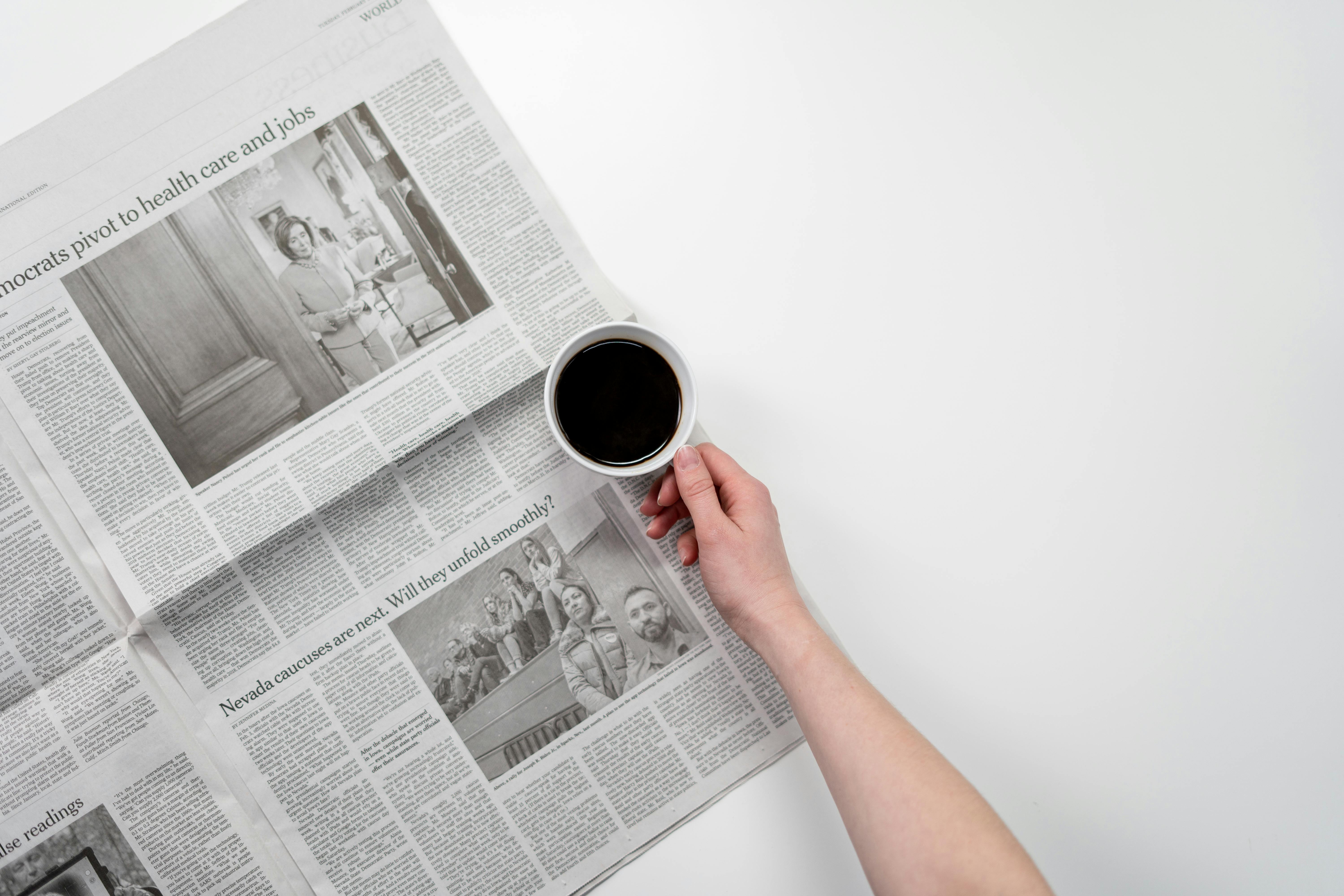 person holding white ceramic mug on newspaper