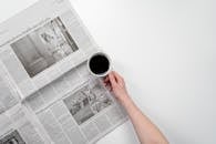 Person Holding White Ceramic Mug on Newspaper