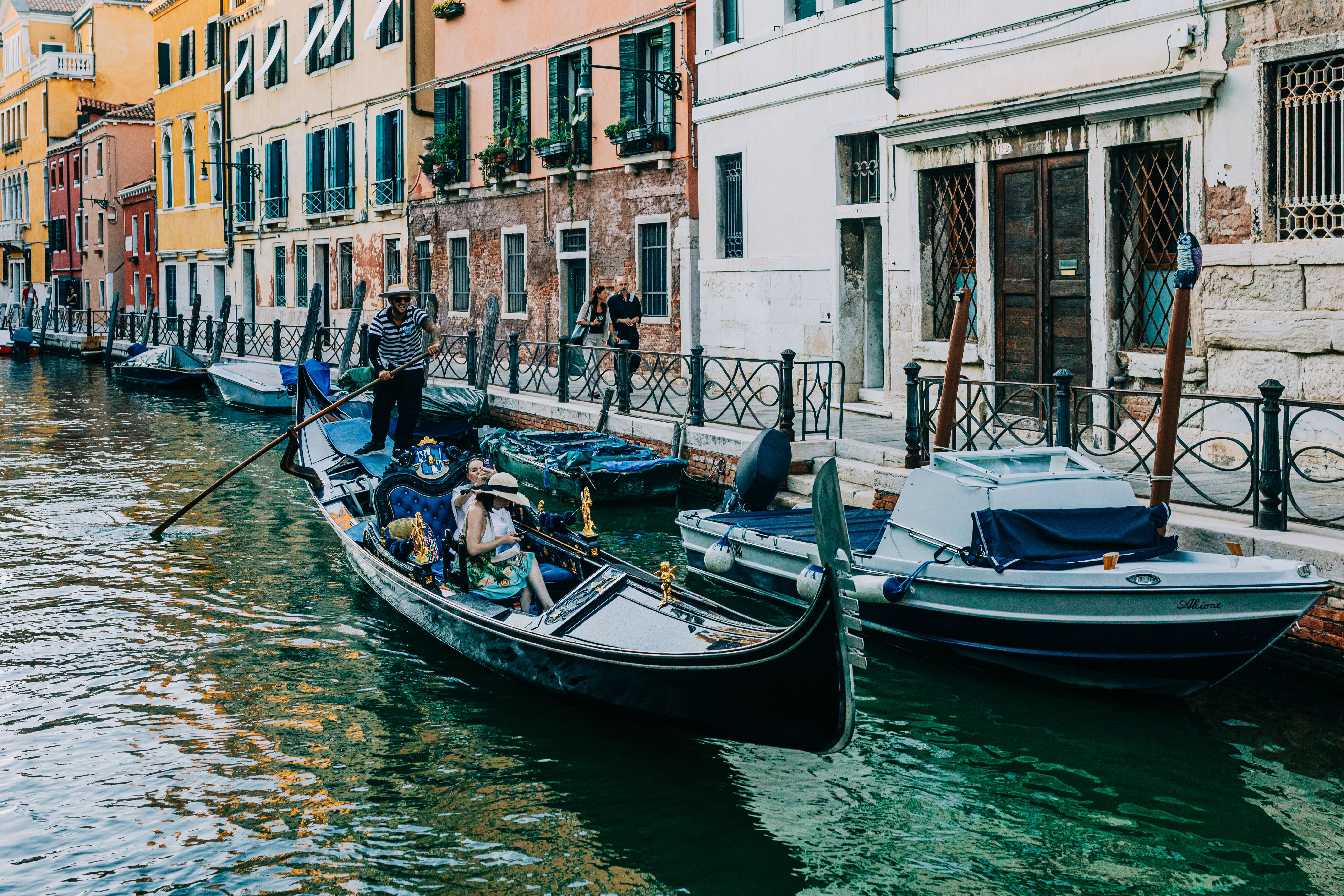 A traditional gondola with tourists navigating through a picturesque canal in Venice, Italy.