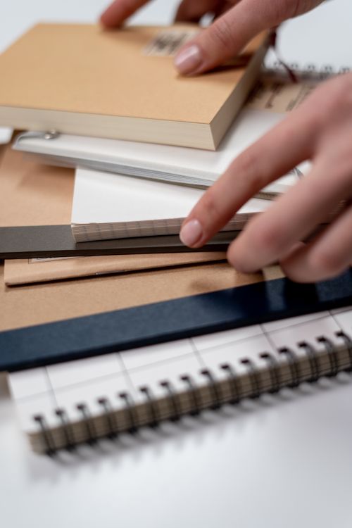 Free Close-up of a hand arranging notebooks and stationery on a desk, perfect for freelance and home office themes. Stock Photo