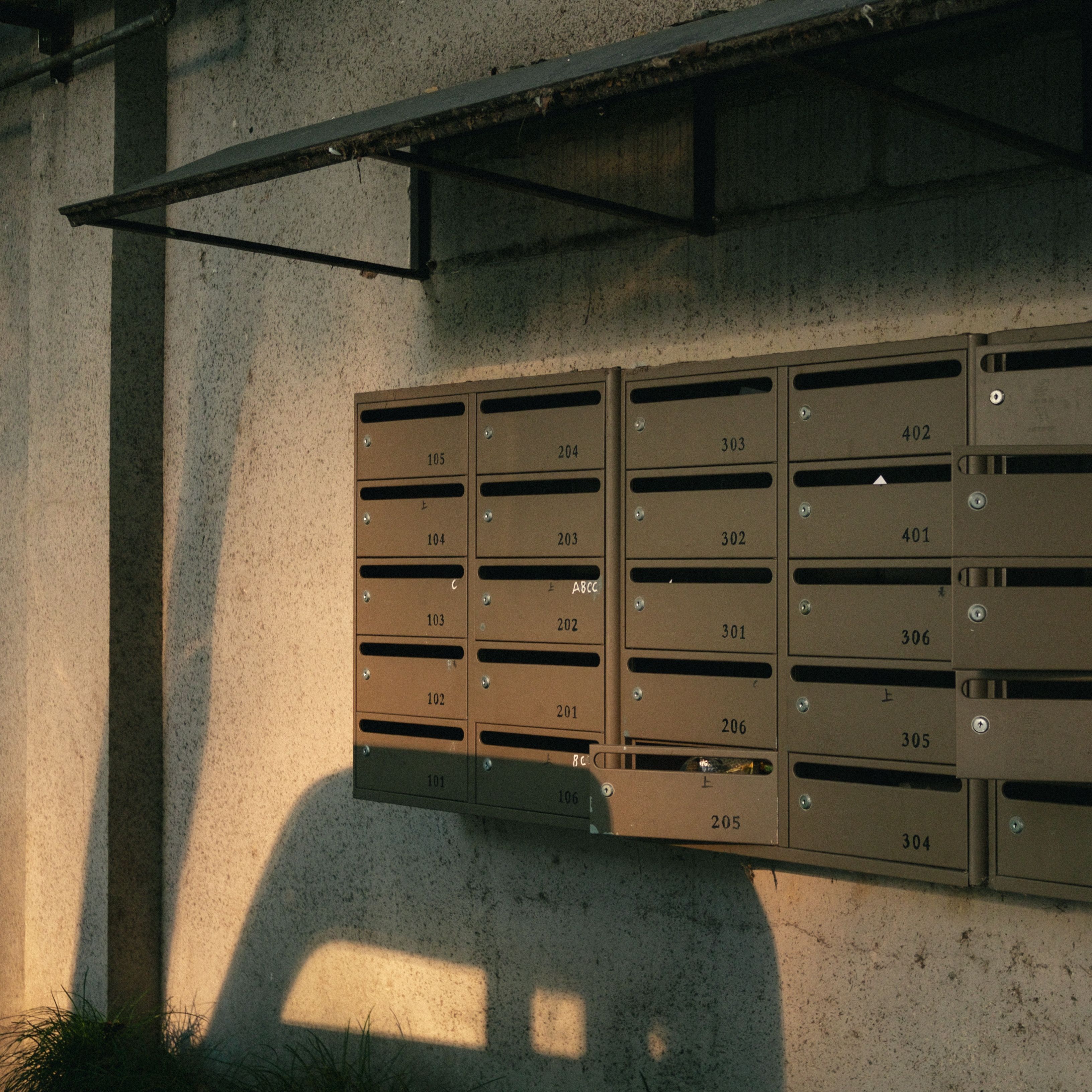 A row of apartment mailboxes illuminated by warm evening light, casting shadows on a concrete wall.