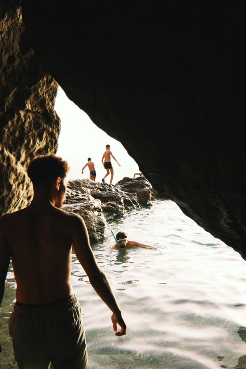 Free Group of young men swimming and exploring a rocky seaside cave on a sunny day. Stock Photo
