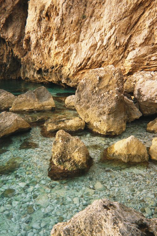 Free Clear turquoise water with sunlit rock formations creating a serene coastal scene. Stock Photo