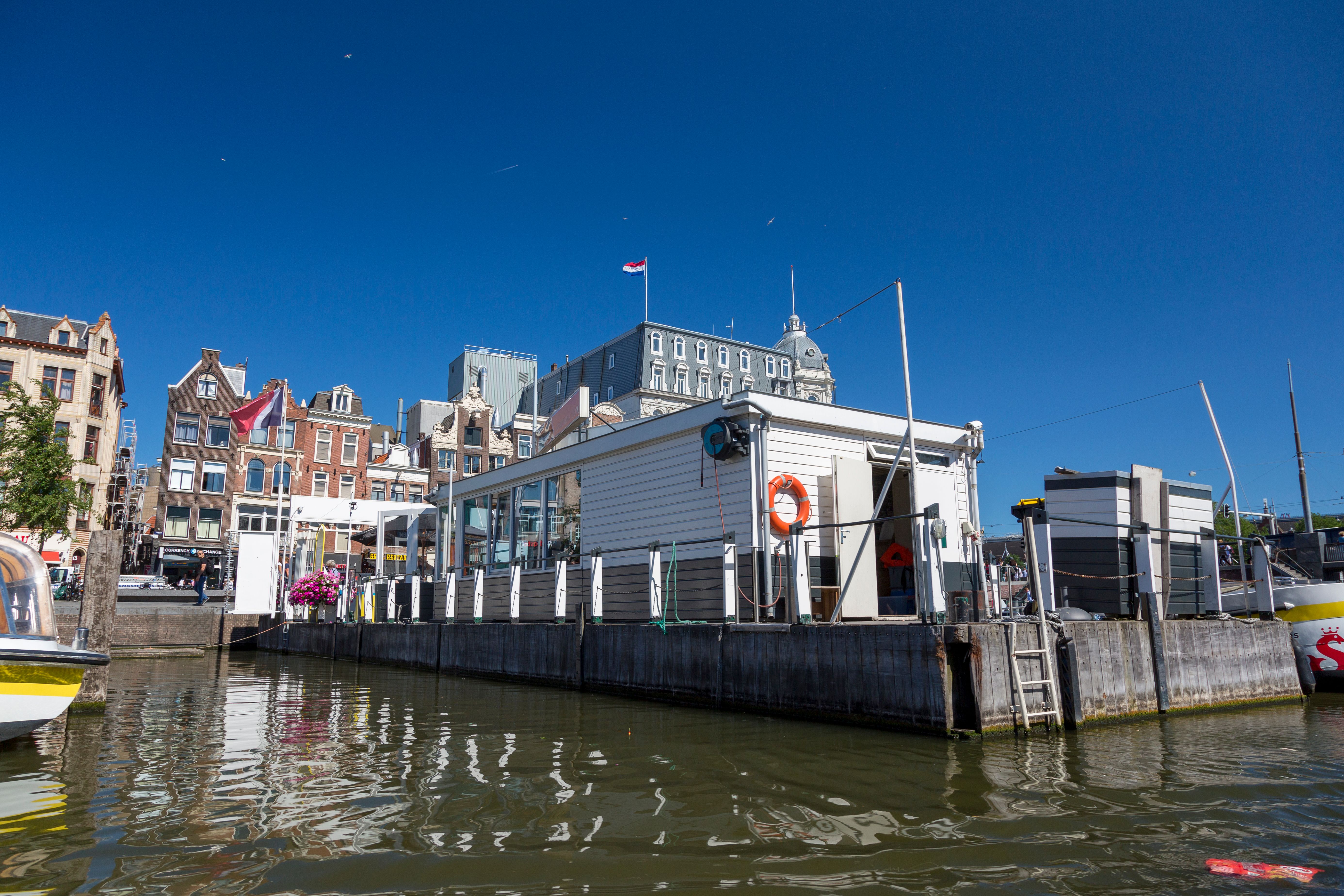 Charming Amsterdam waterfront with architectural buildings and a clear blue sky reflecting in the canal.