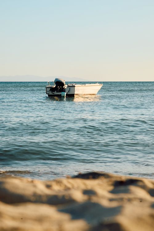 Free A tranquil ocean view with a solitary boat floating near the sandy shore at sunset. Stock Photo
