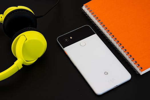 A vibrant flat lay image of a smartphone, yellow headphones, and an orange spiral notebook on a desk.