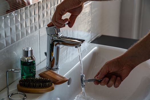 A man's hands adjust the faucet in a bathroom, surrounded by grooming tools like a comb and brush.