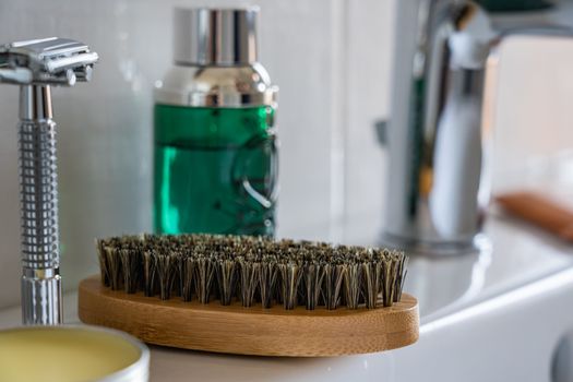 A close-up view of grooming tools, including a shaving brush and razor, on a bathroom sink.