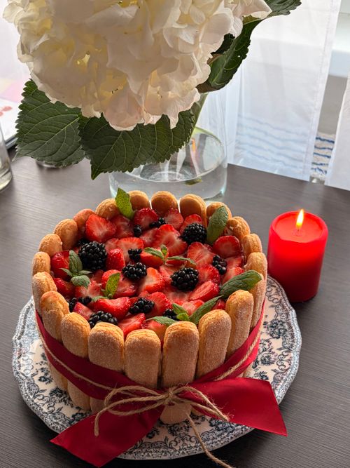 Free Delicious Charlotte cake topped with fresh berries and mint, next to a red candle on a decorated plate. Stock Photo