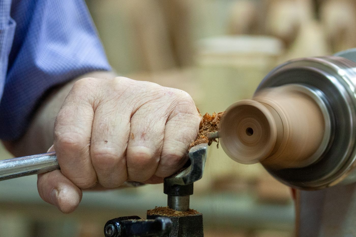 Close-up of craftsman's hand shaping wood on a lathe, showcasing precision and skill.