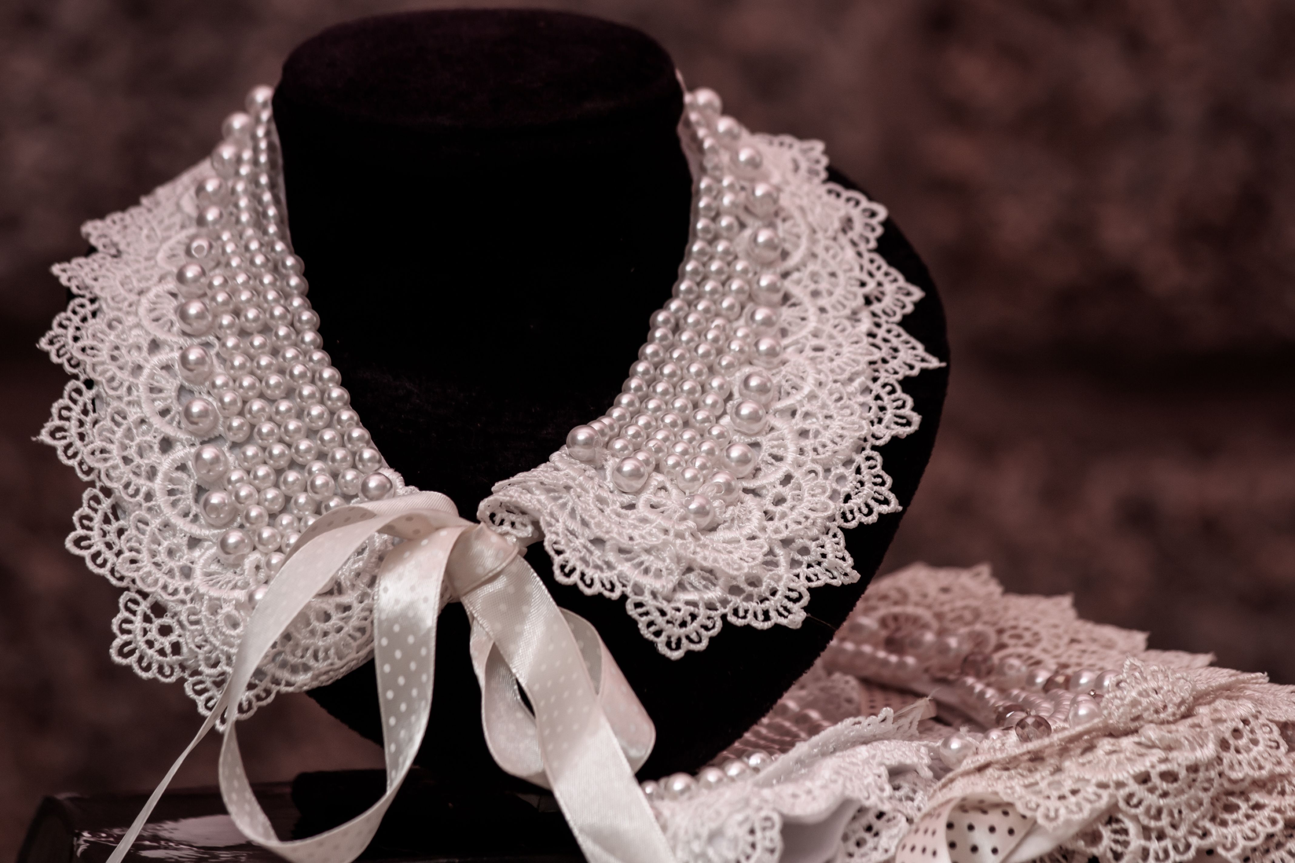 Intricately designed pearl and lace collar on a black stand, perfect for accessorizing.