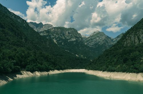 Free Tranquil mountain lake surrounded by lush forests and dramatic peaks under a cloudy sky. Stock Photo