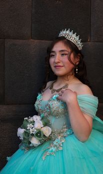 A young woman in a turquoise quinceañera dress holding a bouquet, wearing a tiara.
