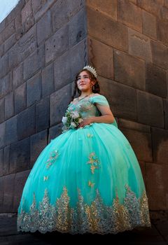 Portrait of a young woman in a turquoise quinceañera dress against a stone wall.