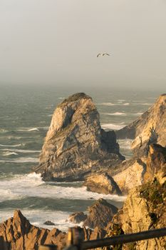 Stunning view of rugged cliffs and ocean waves at sunset in Colares, Portugal.