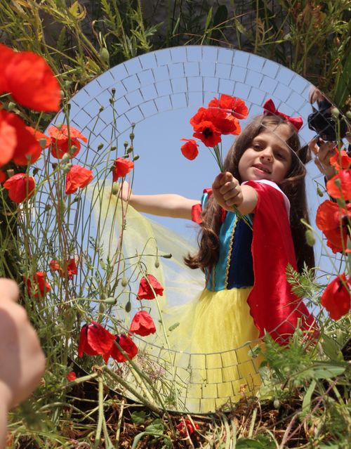 Free Child in costume holding poppies, reflected in a mirror, amidst vibrant nature. Stock Photo