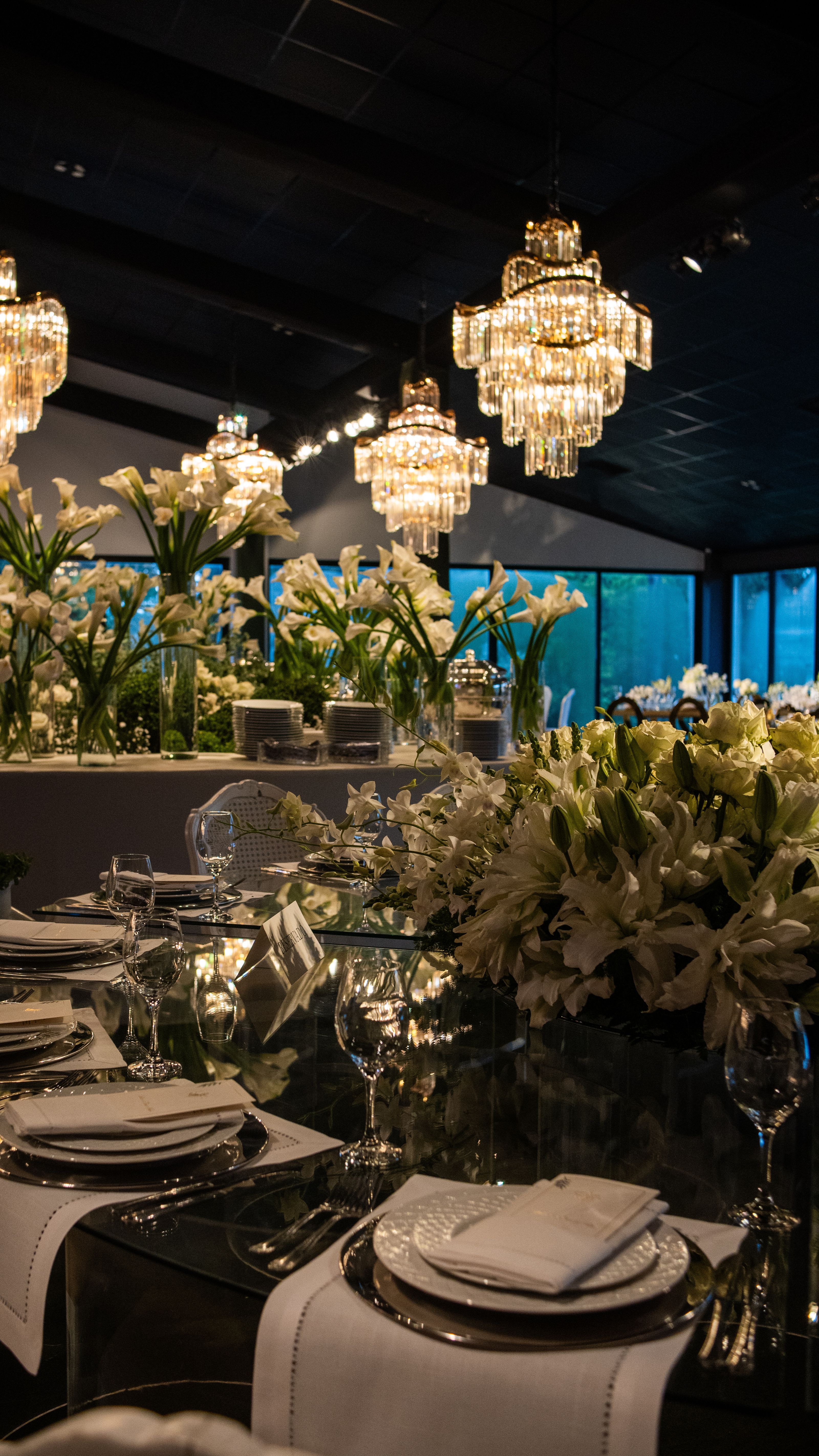 Decoração deslumbrante para a recepção de casamento, com lustres elegantes e arranjos florais de lírios brancos.
