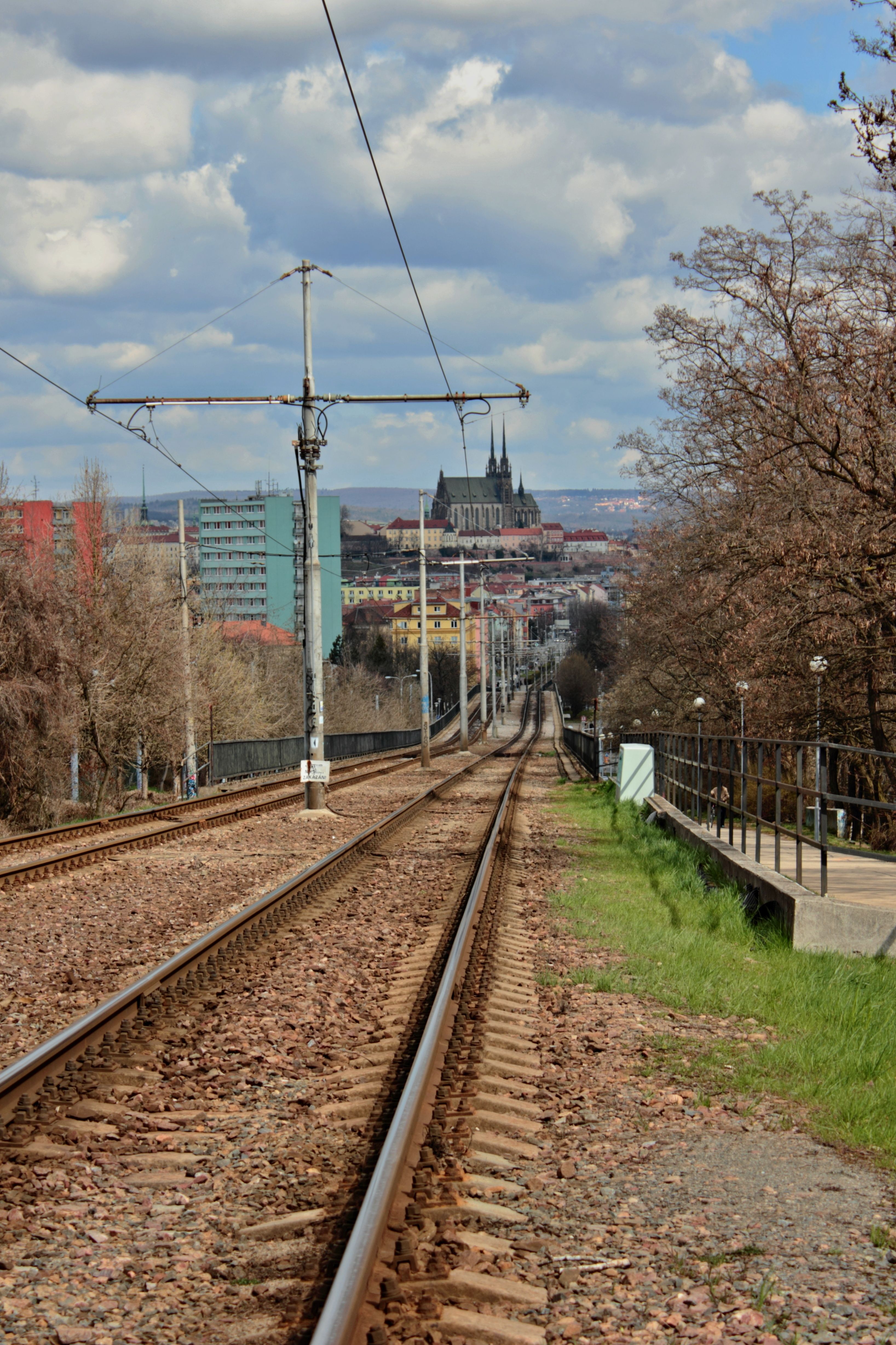 Railway tracks leading towards a city skyline with Brno's cathedral visible, offering a scenic urban view.