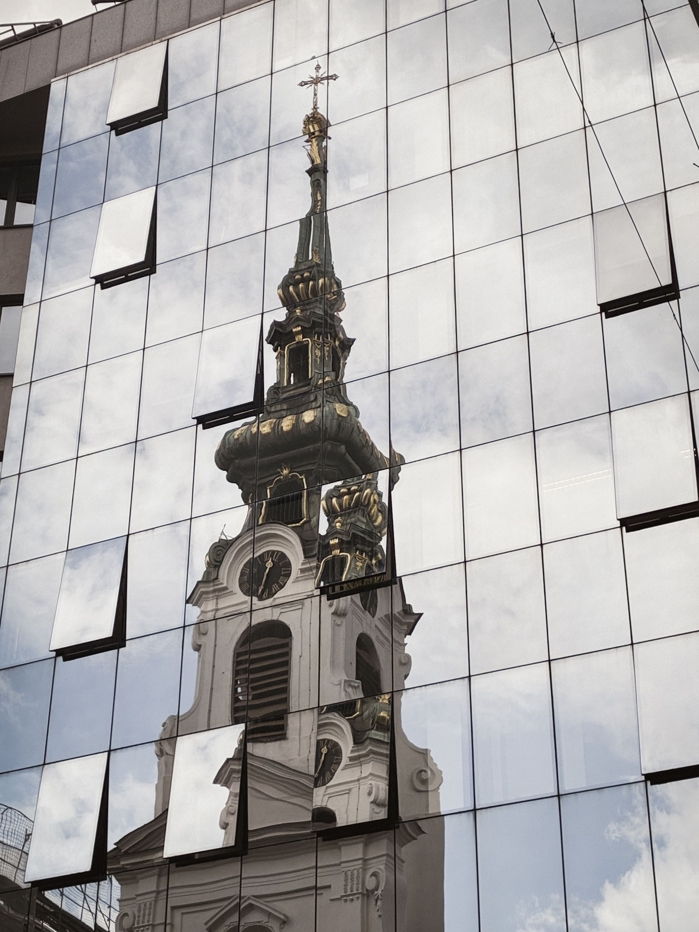 Reflective view of St. Peter's Church with baroque architecture mirrored in a glass facade in Vienna, Austria.