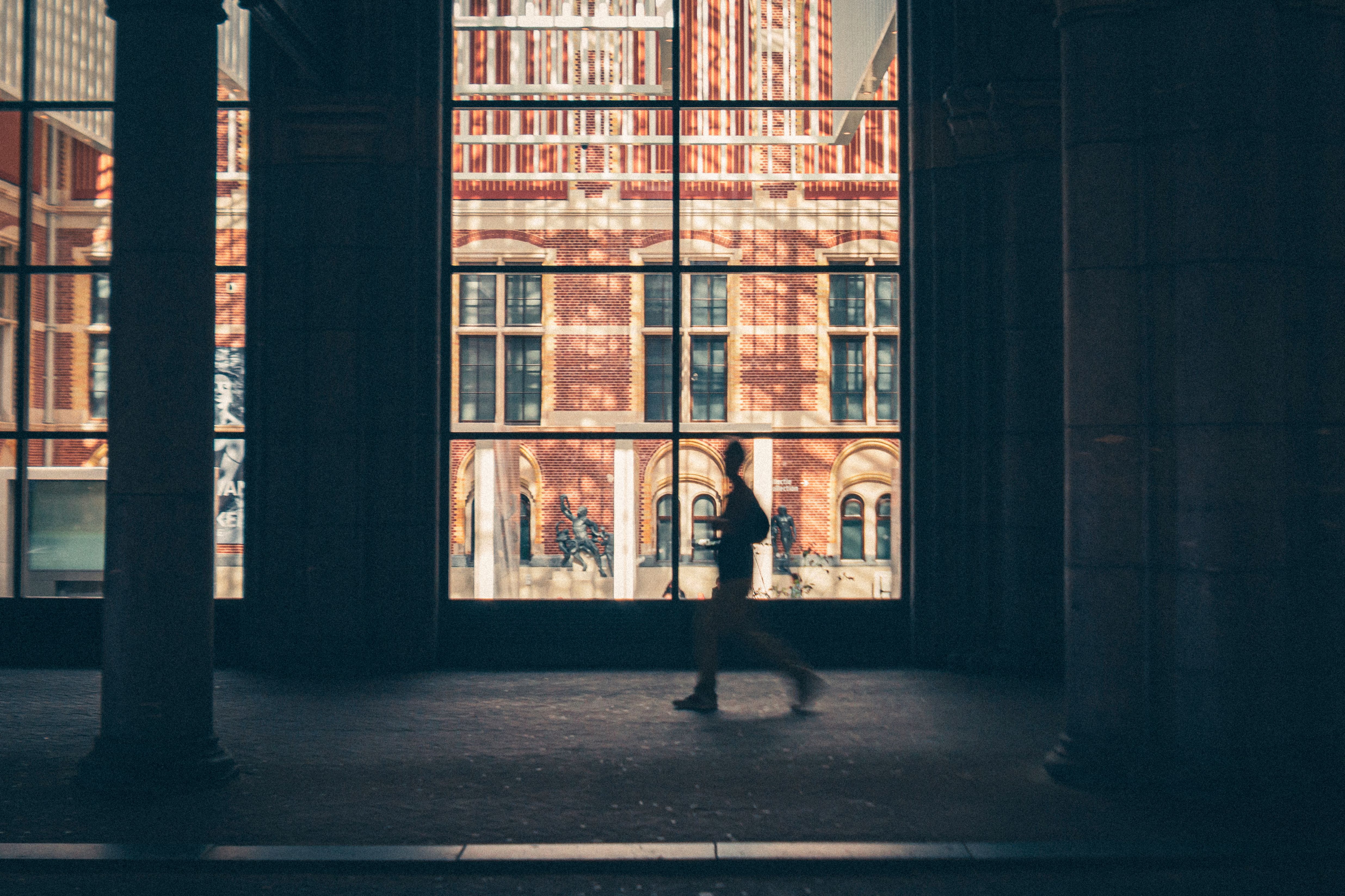 A silhouette of a person walking inside the Rijksmuseum, Amsterdam, with a view of historic architecture.