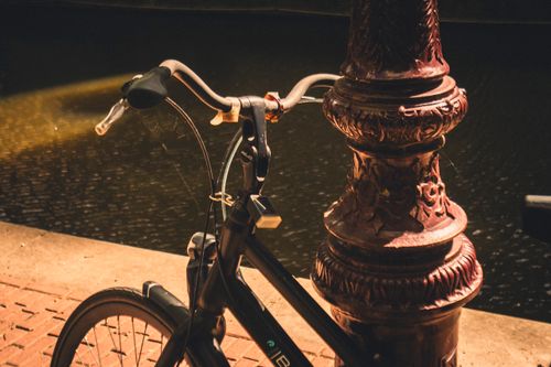Free A vintage bicycle parked beside an ornate lamp post along an Amsterdam canal, bathed in warm evening light. Stock Photo