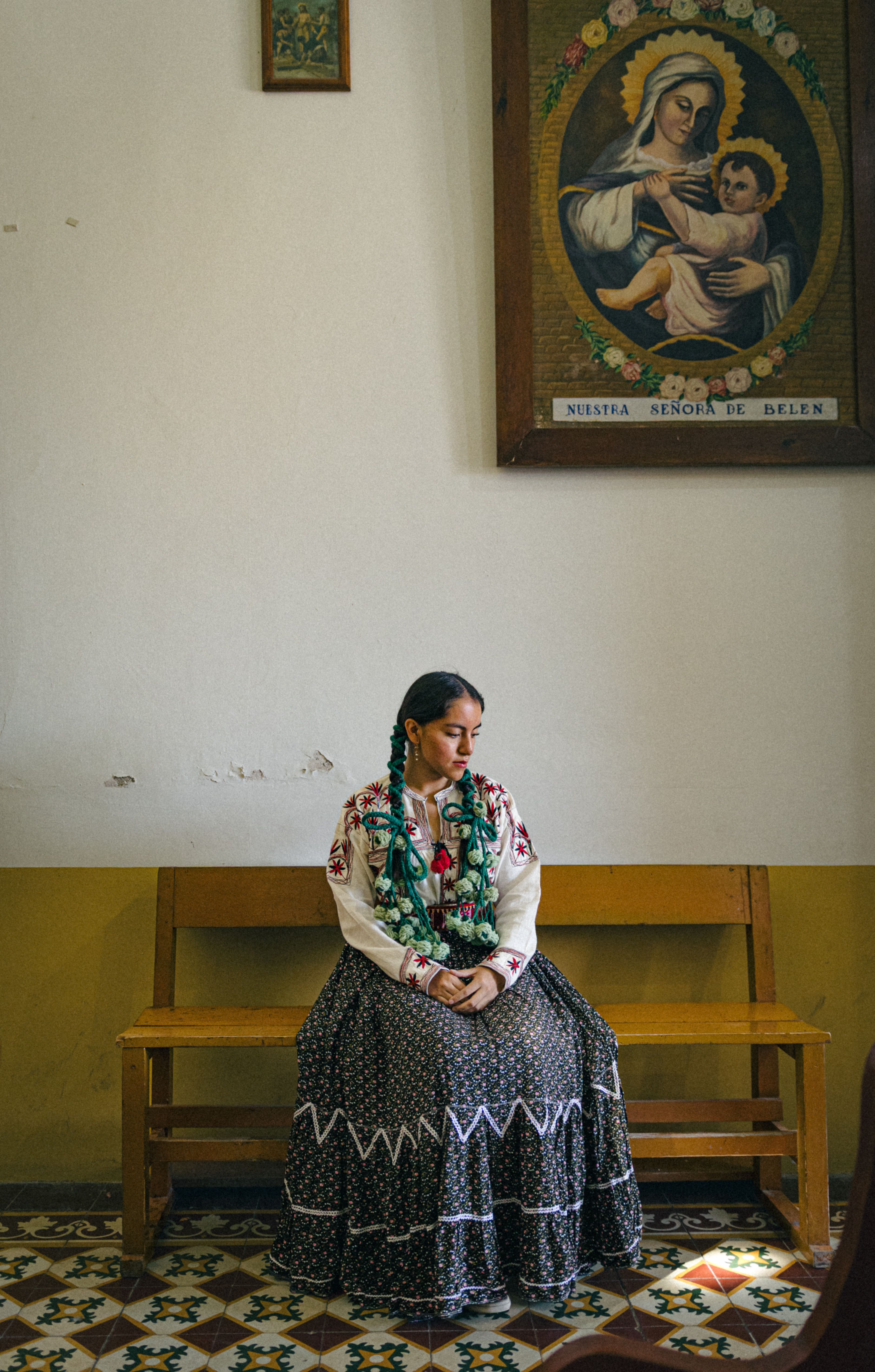 A young woman wearing traditional attire sits thoughtfully in a church interior.