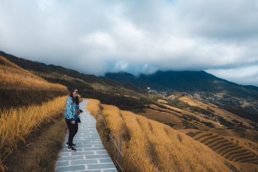 A woman stands by the Longsheng Rice Terraces in Guilin, China, capturing the stunning fall landscape.