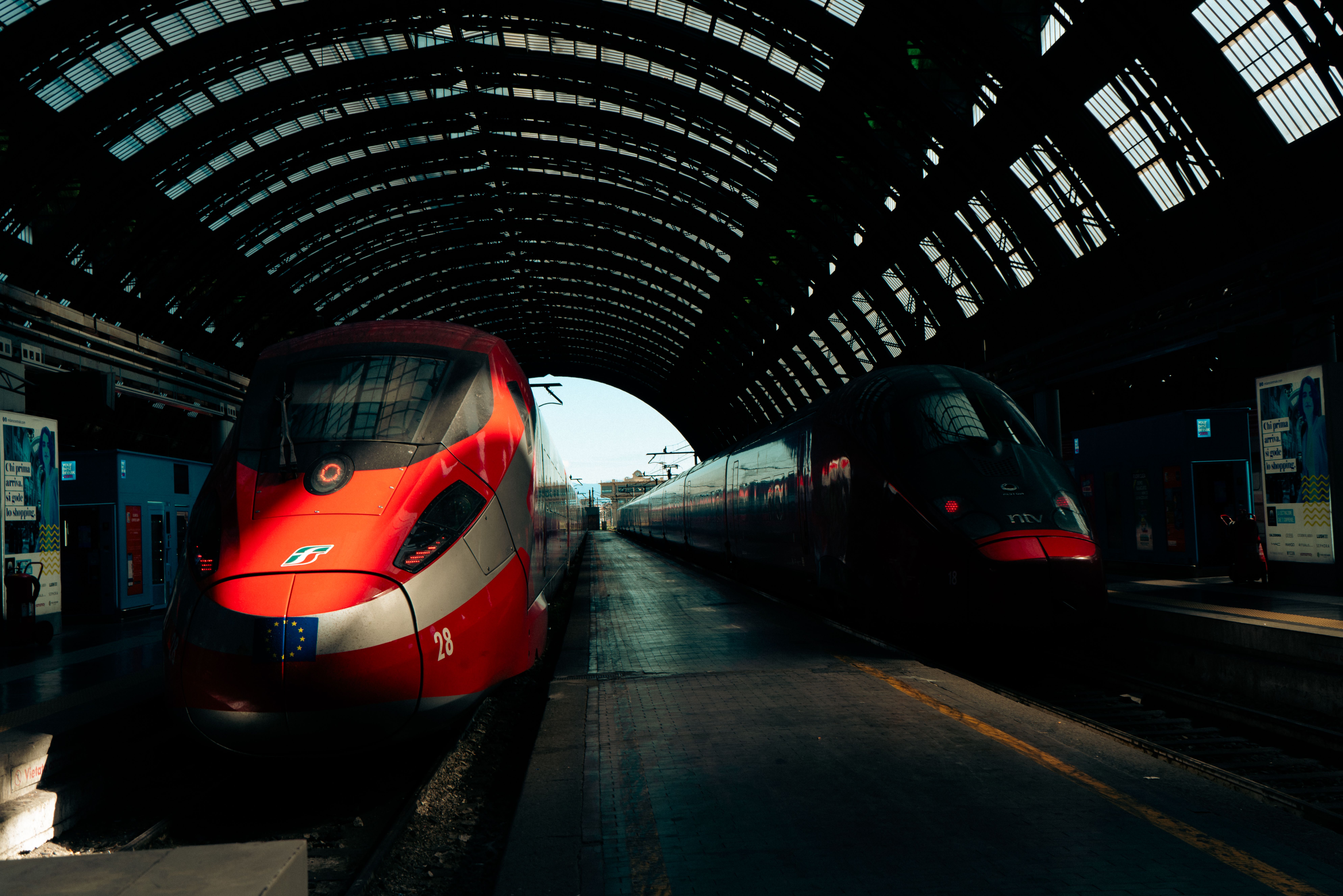 Dynamic view of high-speed trains in iconic Milan Central Station under a glass roof.