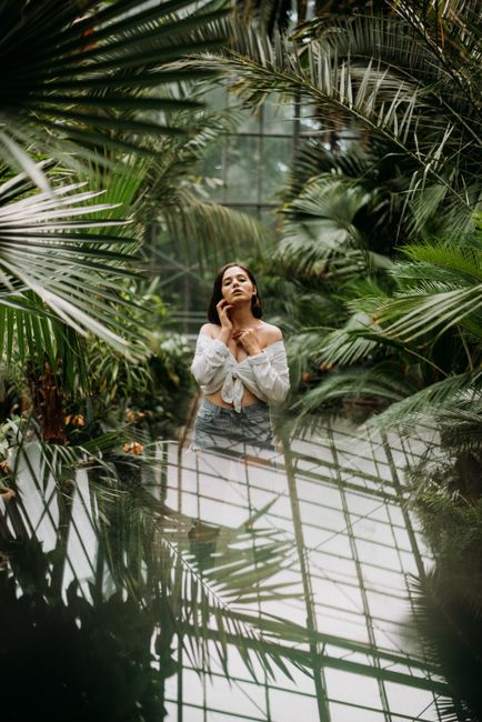 A woman stands gracefully amidst tropical plants in a greenhouse, evoking tranquility.