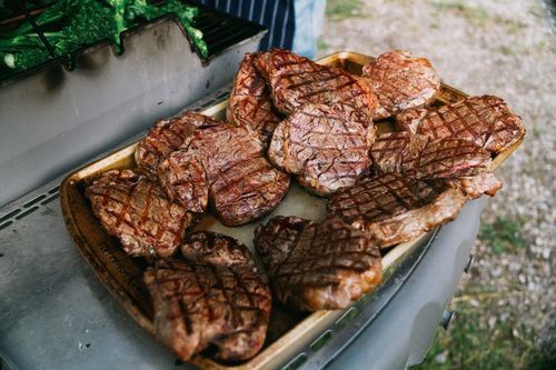 Free Delicious grilled steaks on a tray next to green vegetables on an outdoor barbecue. Stock Photo