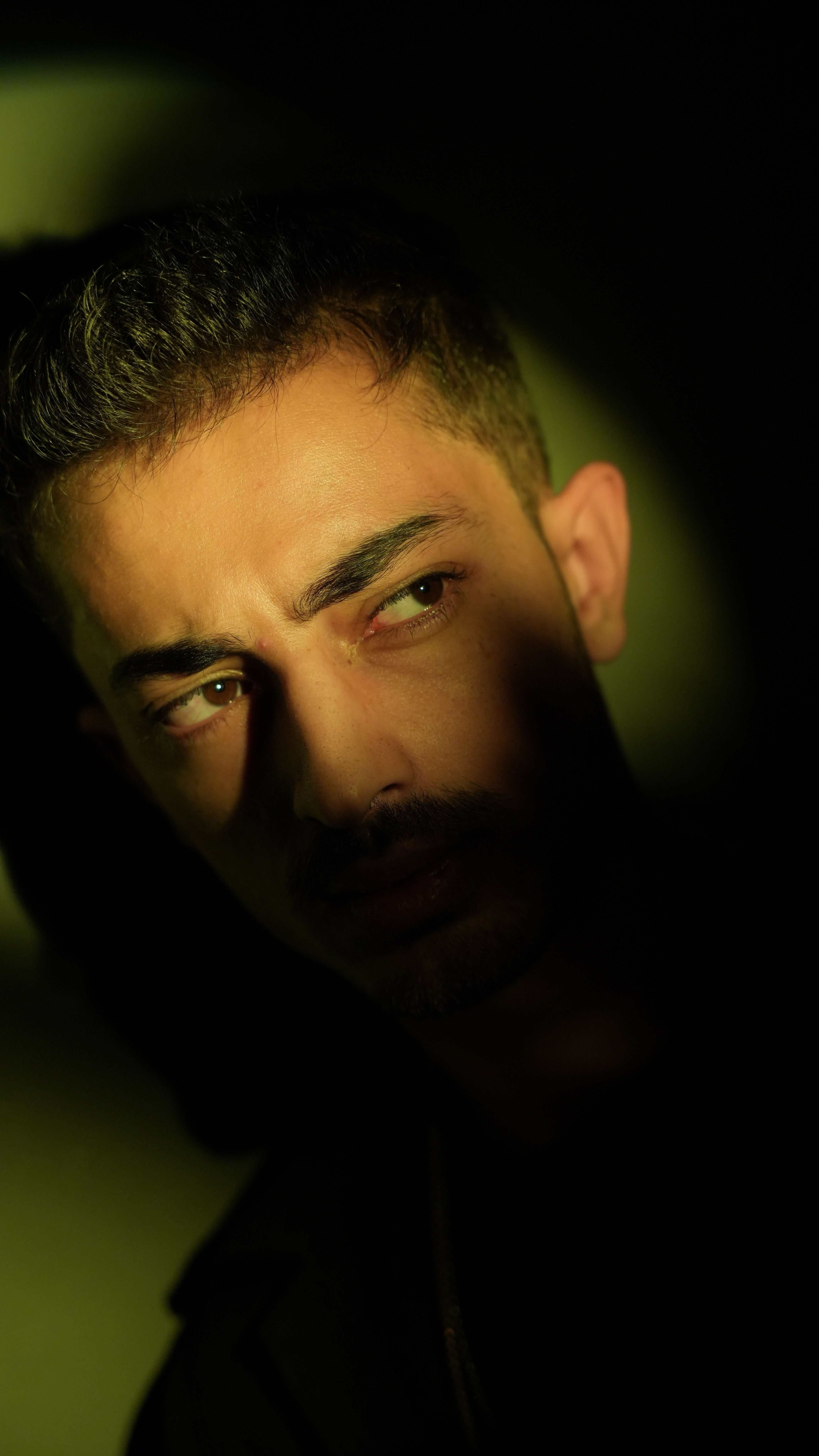 A dramatic low-key portrait capturing a young man in a contemplative mood with chiaroscuro lighting.