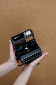 Hands holding a classic vintage Polaroid camera in front of a cork background.