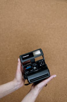 Close-up of hands holding a vintage Polaroid camera with a cork background.