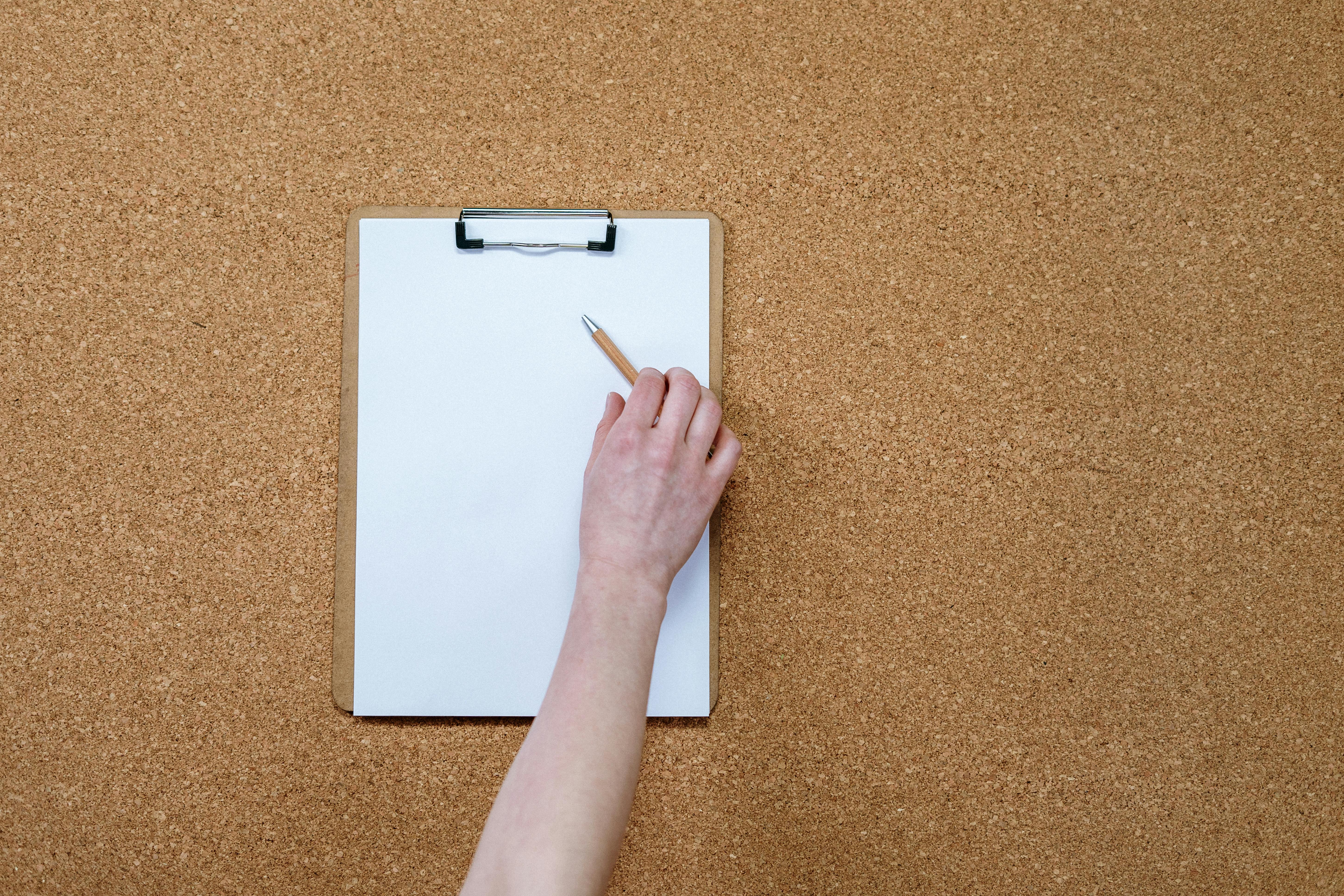 Close-up of a hand writing on a clipboard against a corkboard background, perfect for business or planning themes.