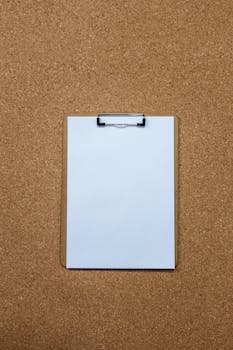A blank clipboard placed on a cork board surface, perfect for productivity themes.