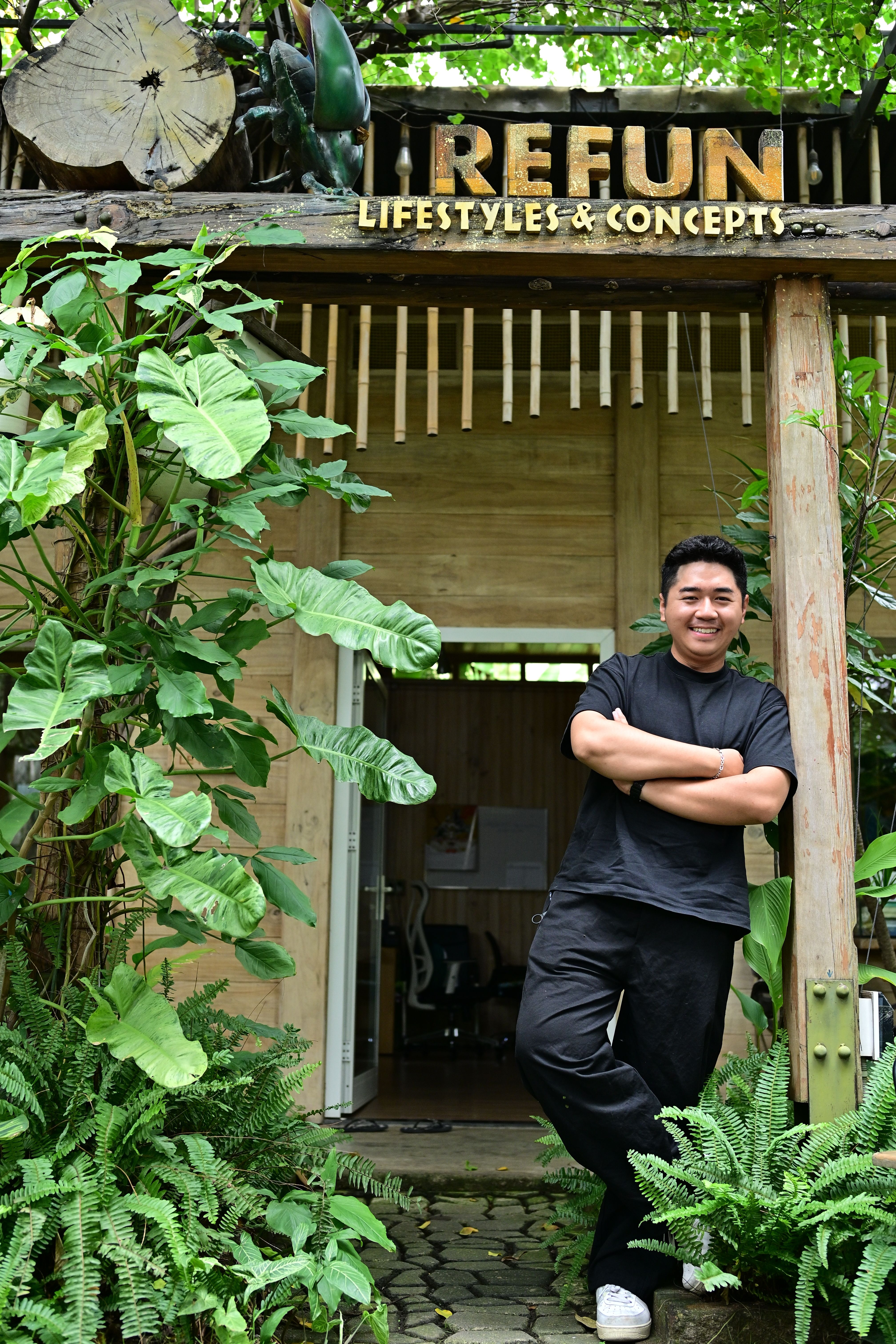 Young man standing confidently at the entrance of an eco-friendly shop with lush greenery.